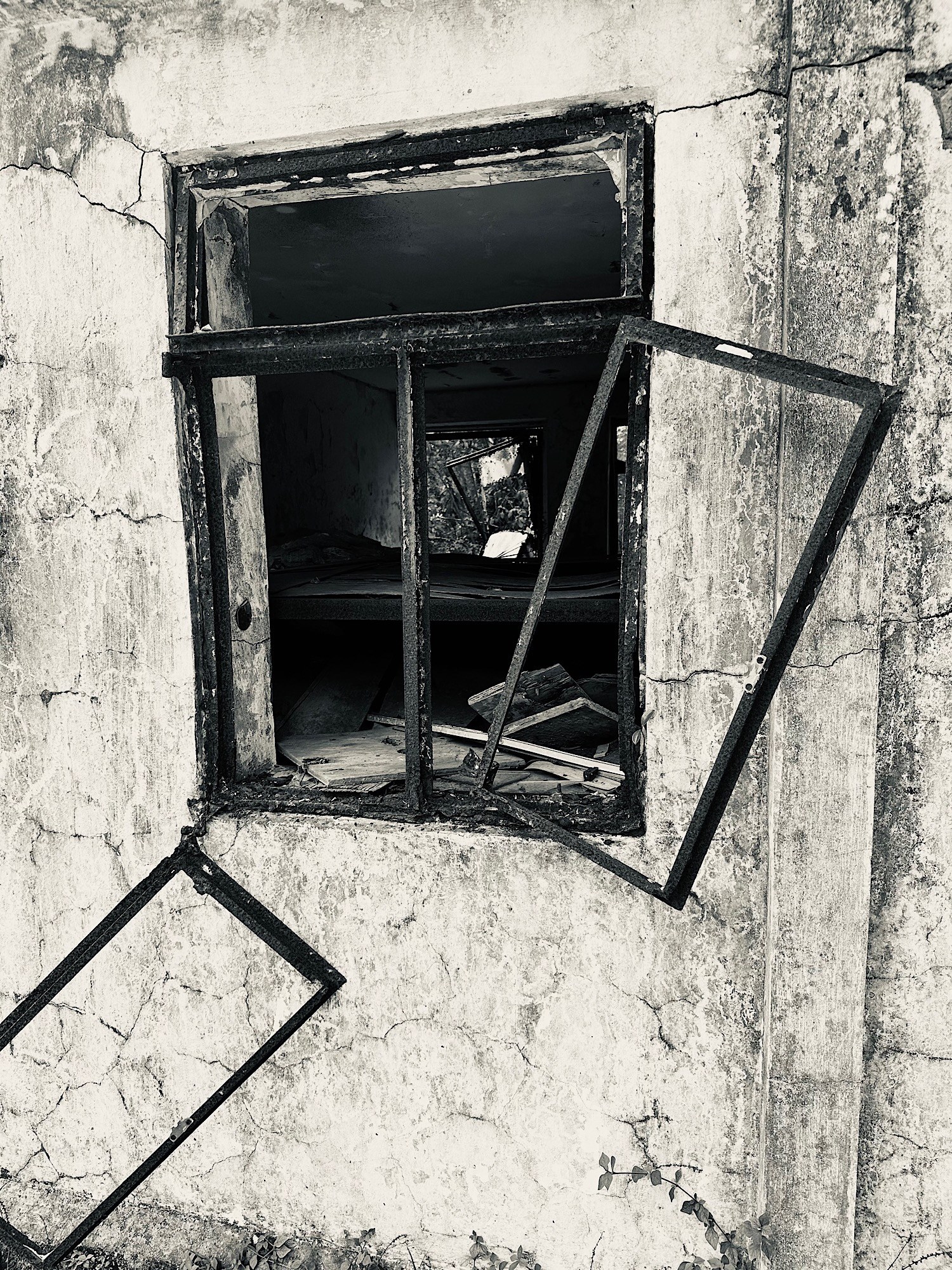 A broken metal window frame swings outward from a cracked, weathered wall and dark interior.