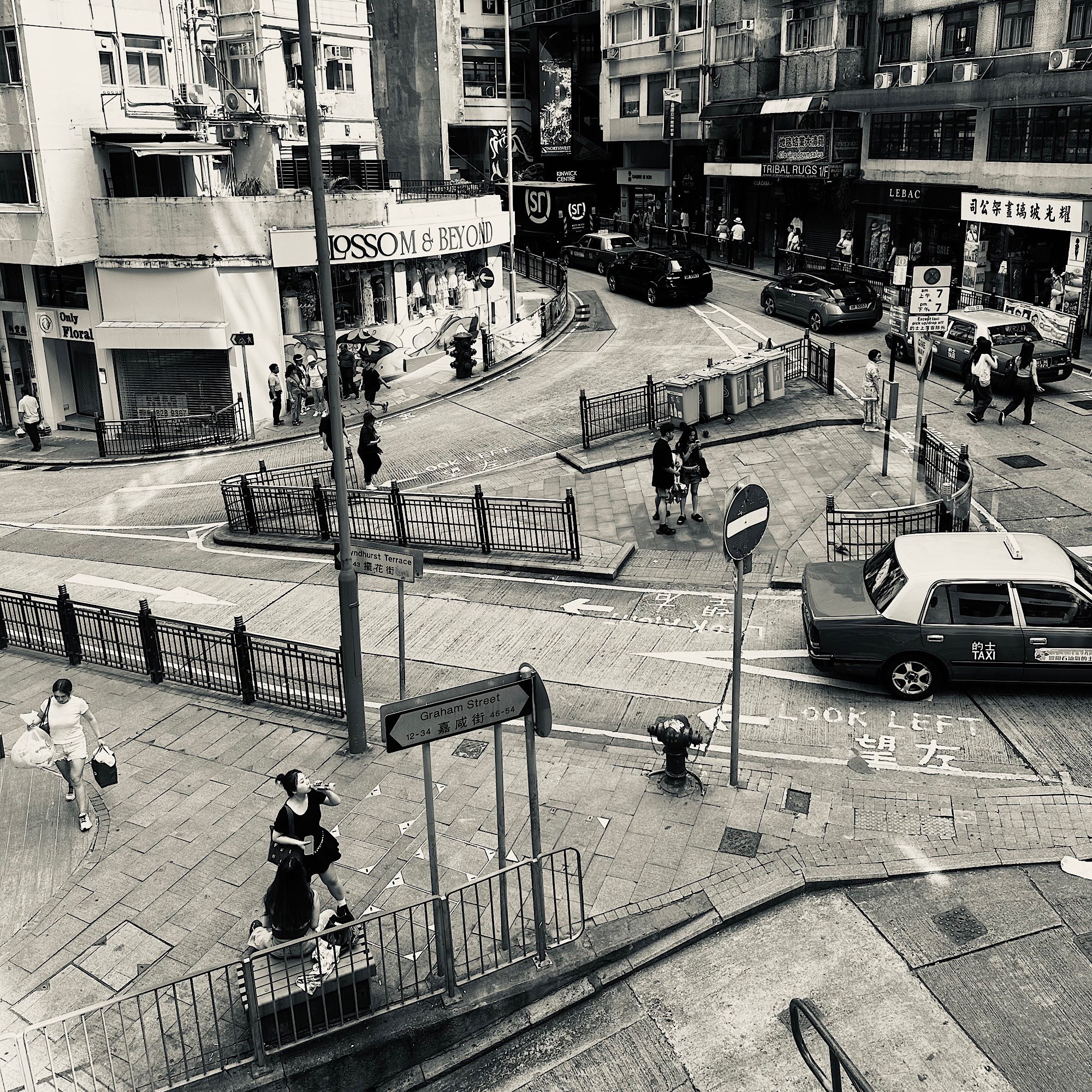 An elevated Hong Kong intersection with taxis, railings, bilingual signs and pedestrians moving in several directions.