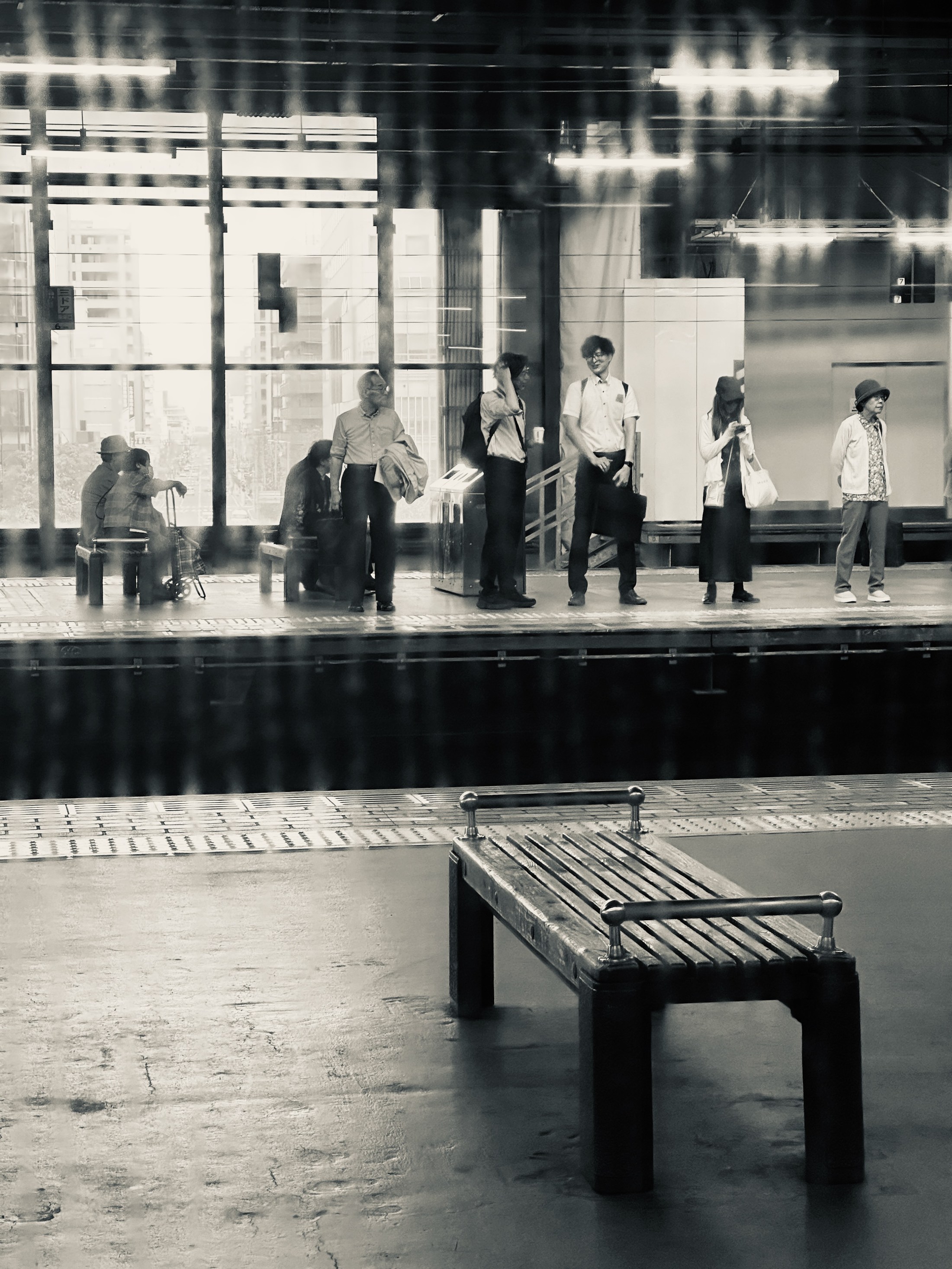 An empty station bench with distant passengers waiting beyond it.