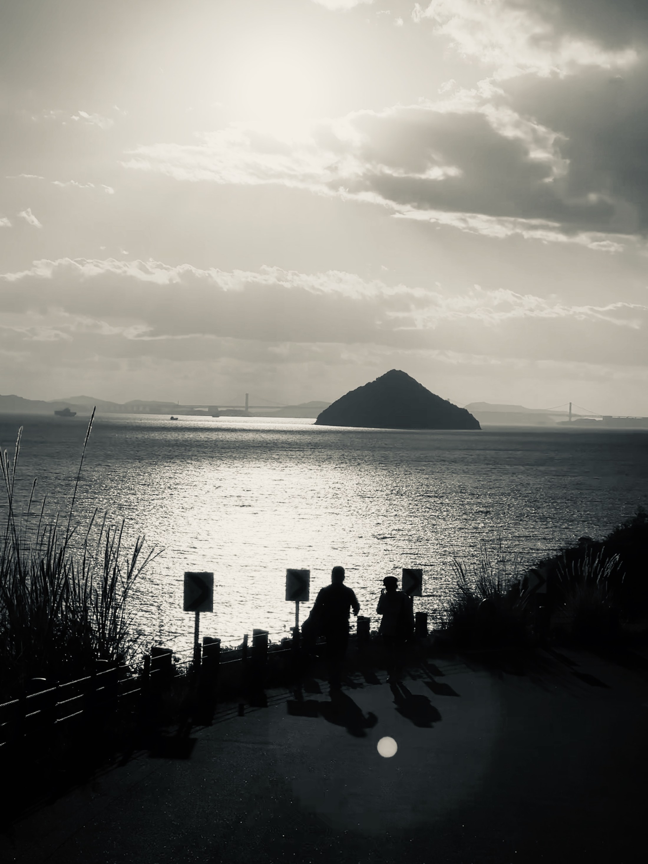 Small silhouetted figures at the water’s edge with a distant rock on the horizon.