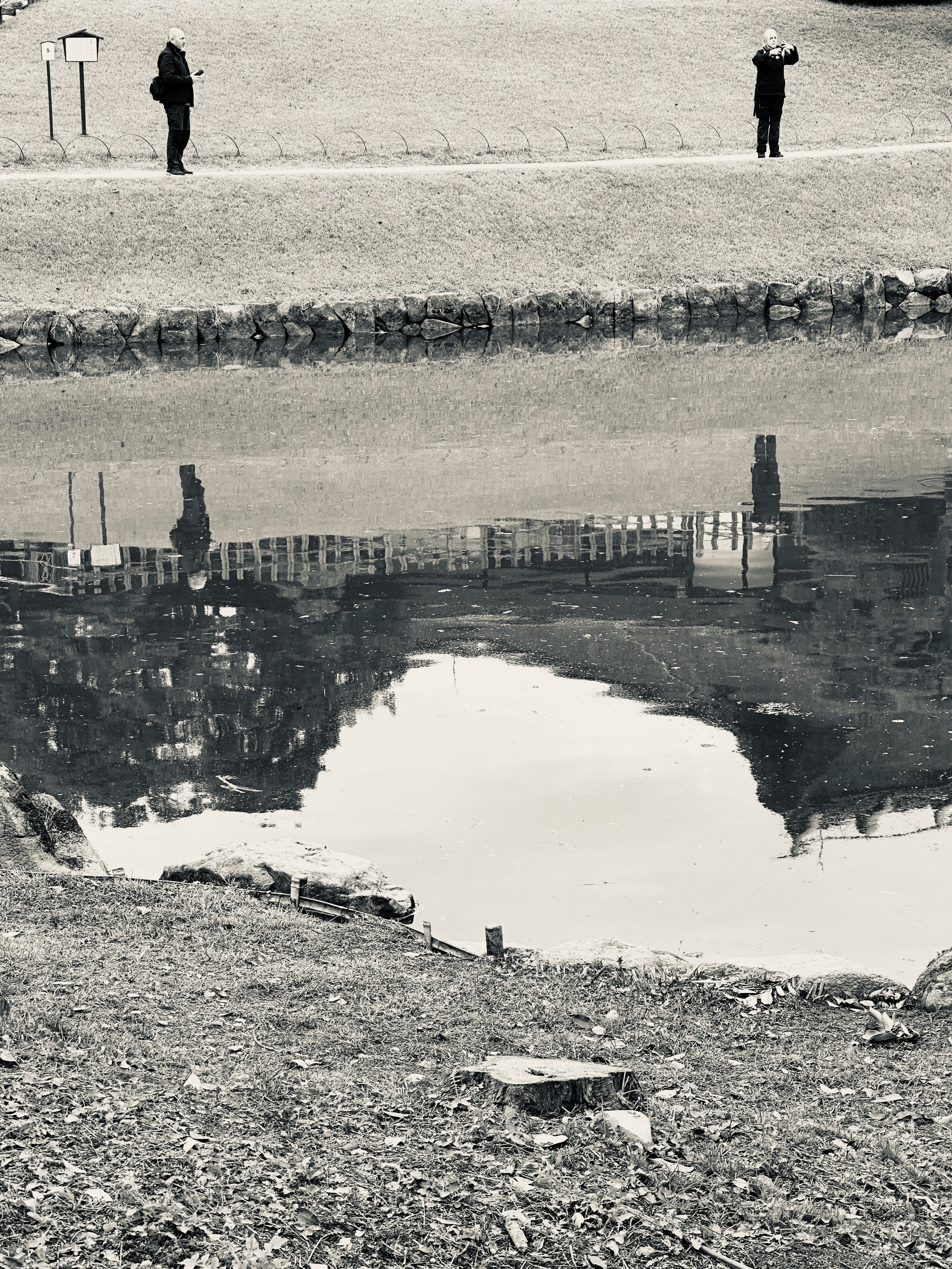 A shoreline and spaced figures inverted in a broad pool of still water.