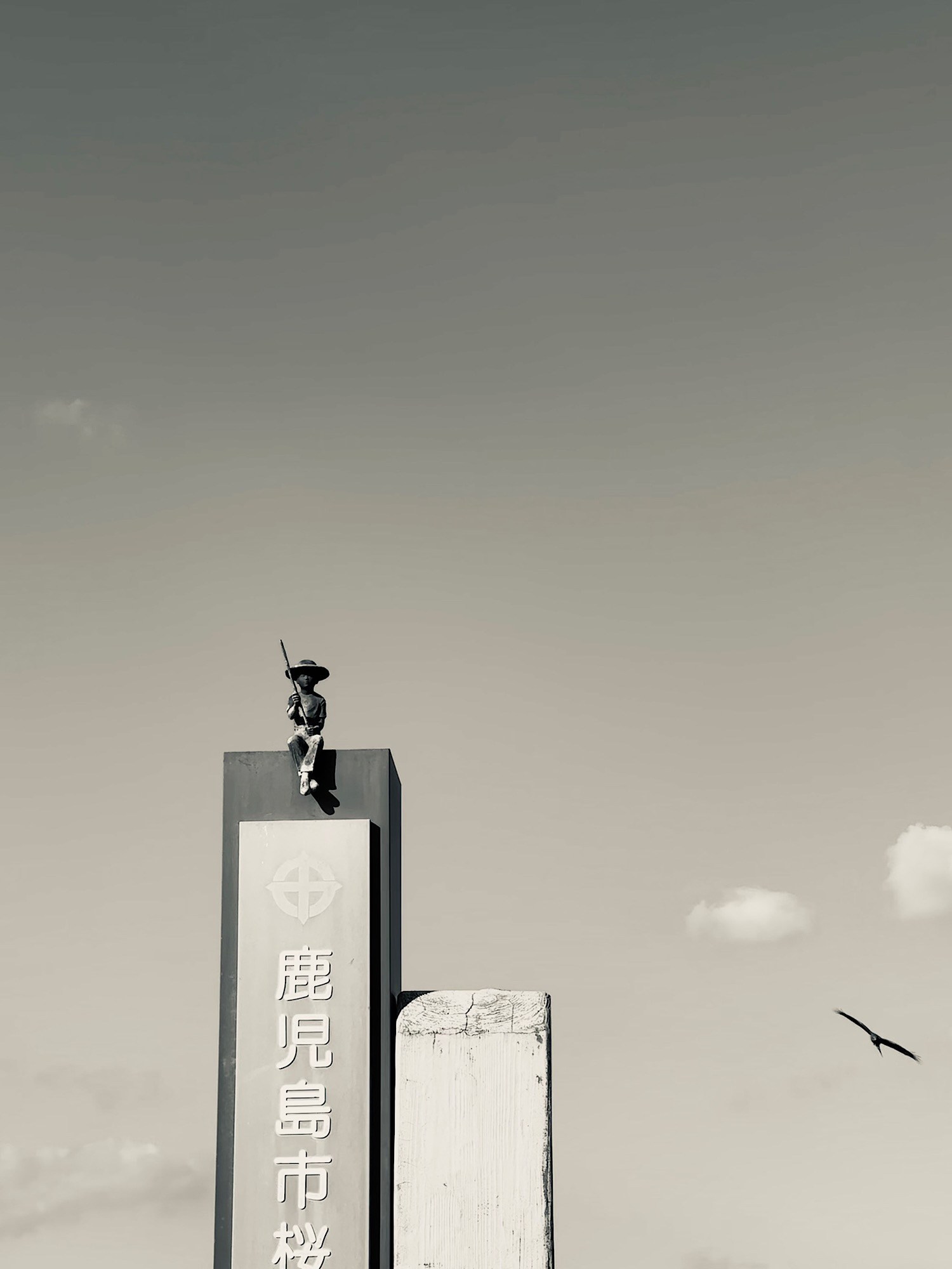 Two birds punctuate a pale sky beside a tall marker inscribed with Japanese characters.