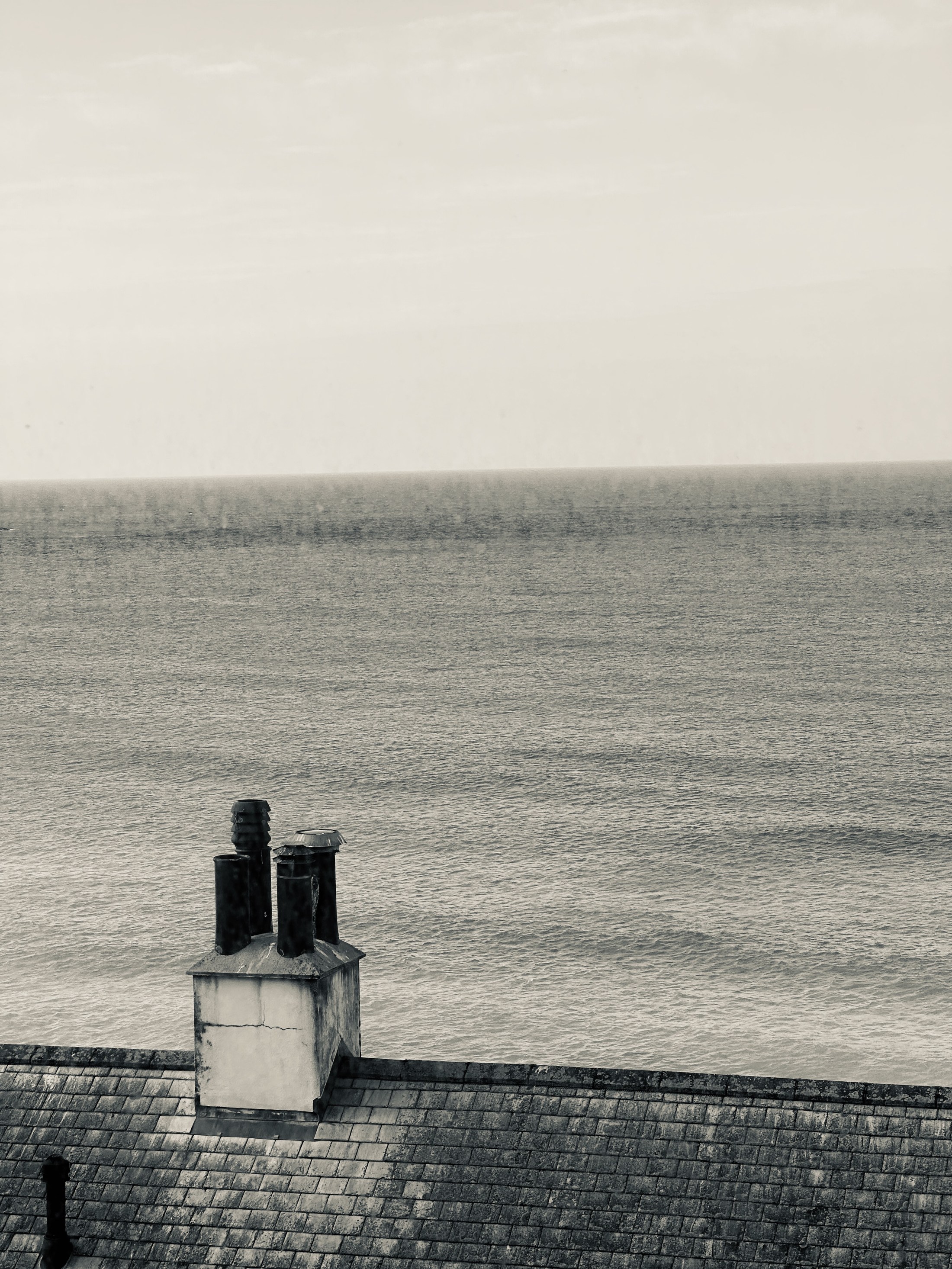 Rooftop chimneys set against a distant horizontal strip of sea.
