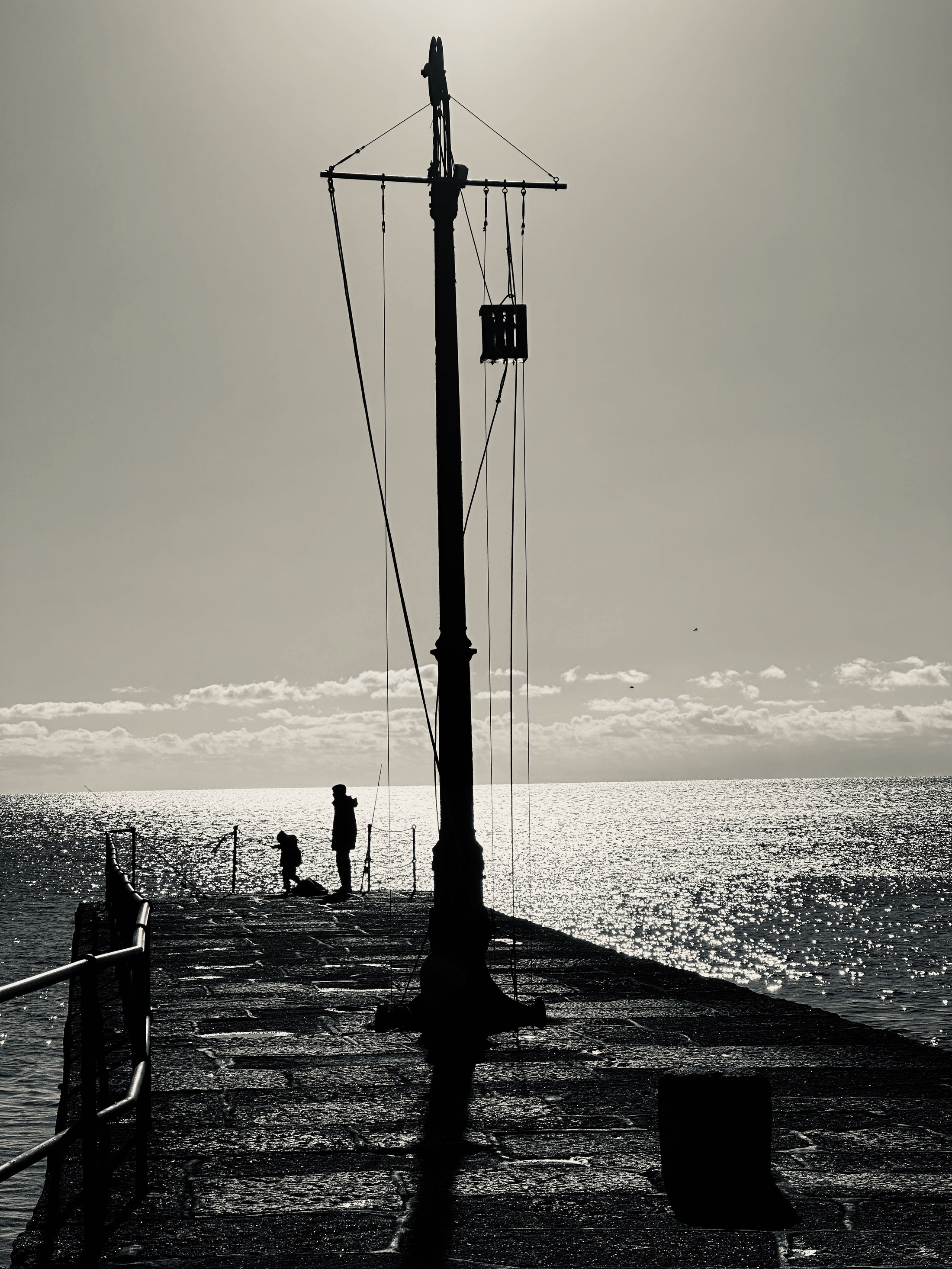 A tall pier hoist silhouetted against the sea and bright sky.