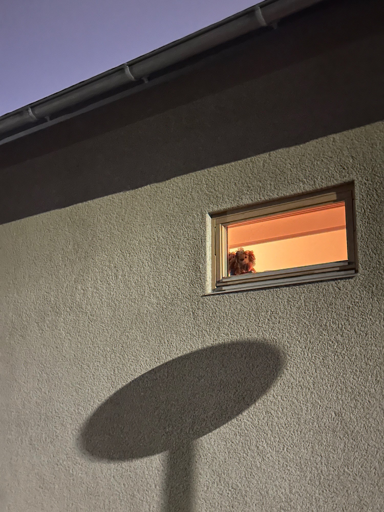 A warm rectangular window sits within a vast oval shadow on a pale wall.