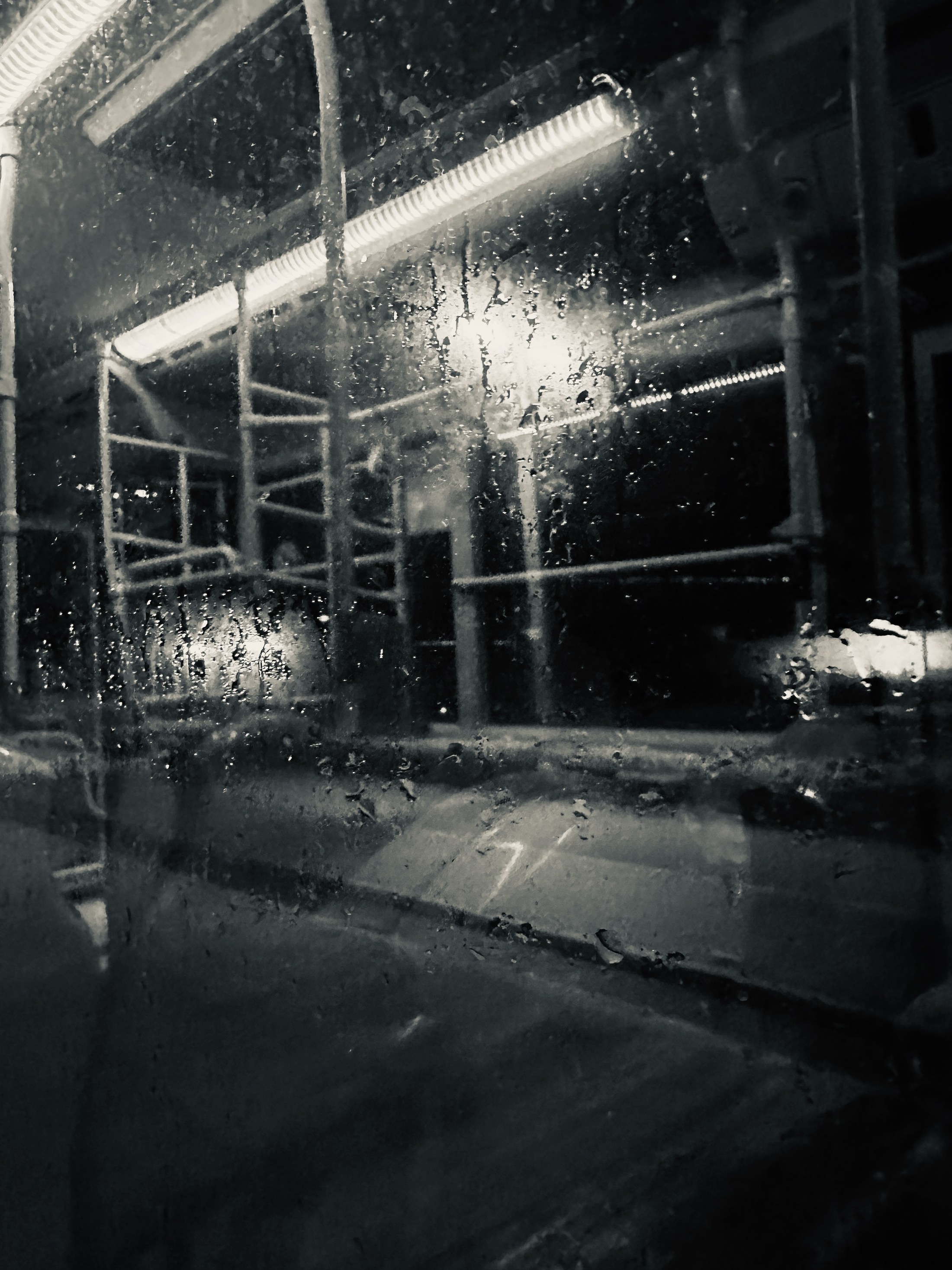 An empty transit interior and points of night light seen through rain-beaded glass.