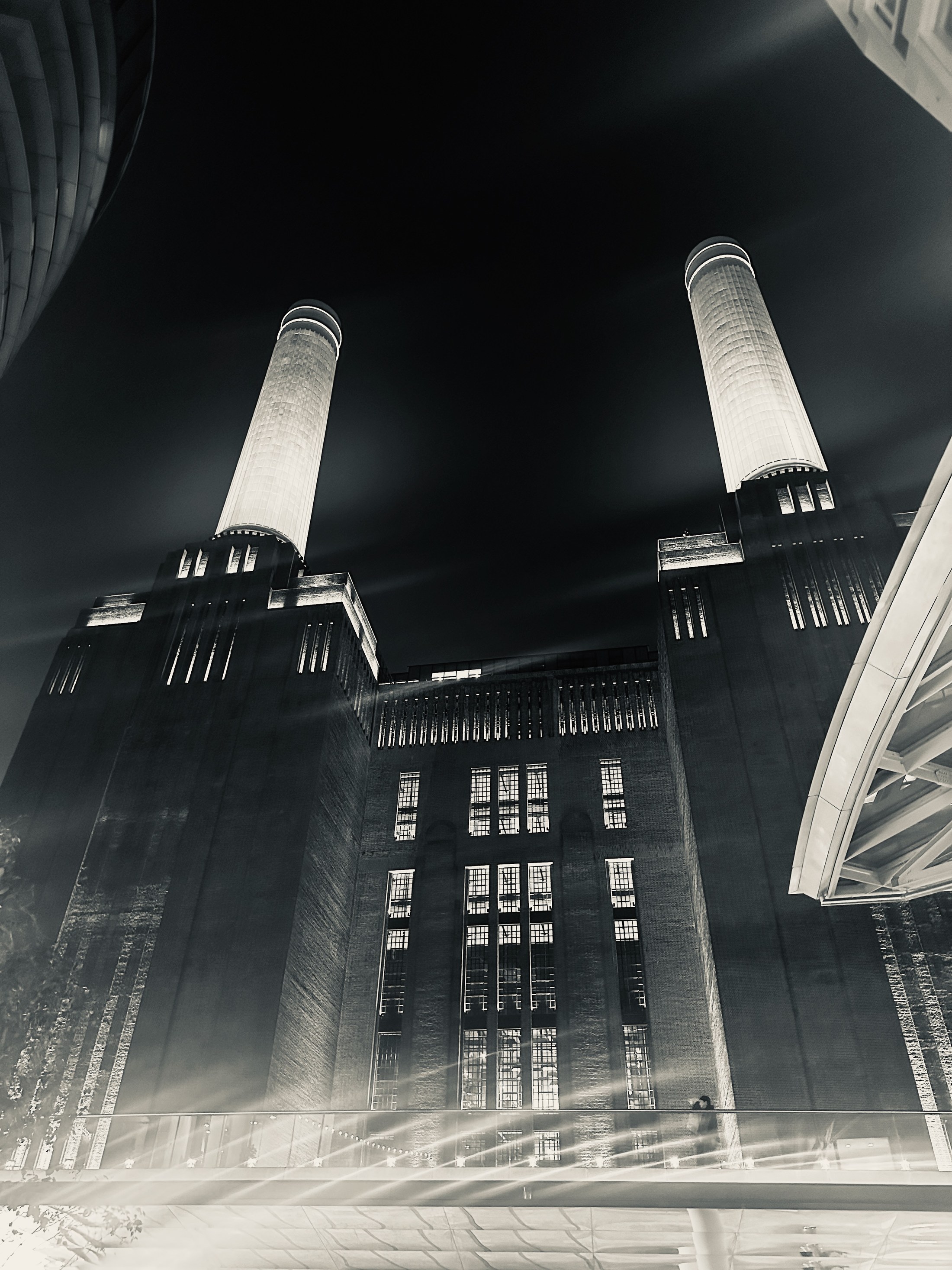 Two illuminated chimney stacks rising above the dark brick façade of Battersea Power Station.