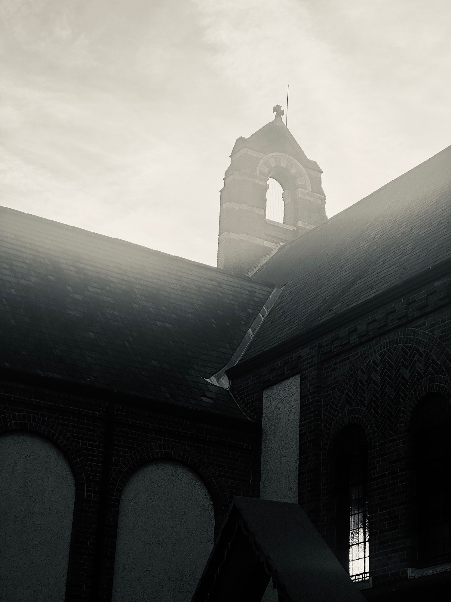 A dark tower rises in backlight between steep tiled roofs.