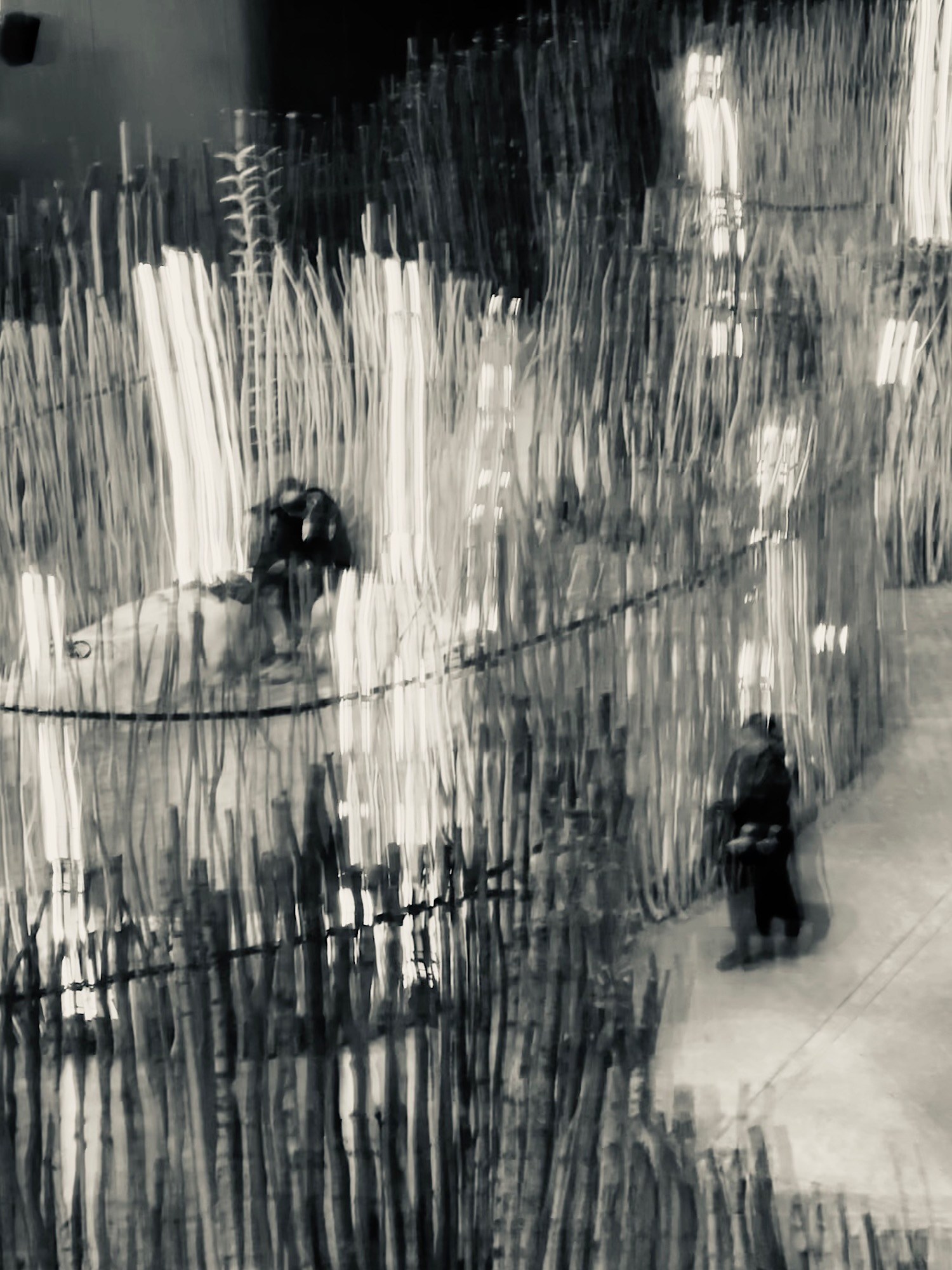 Two moving figures veiled by long vertical trails of rain on glass.