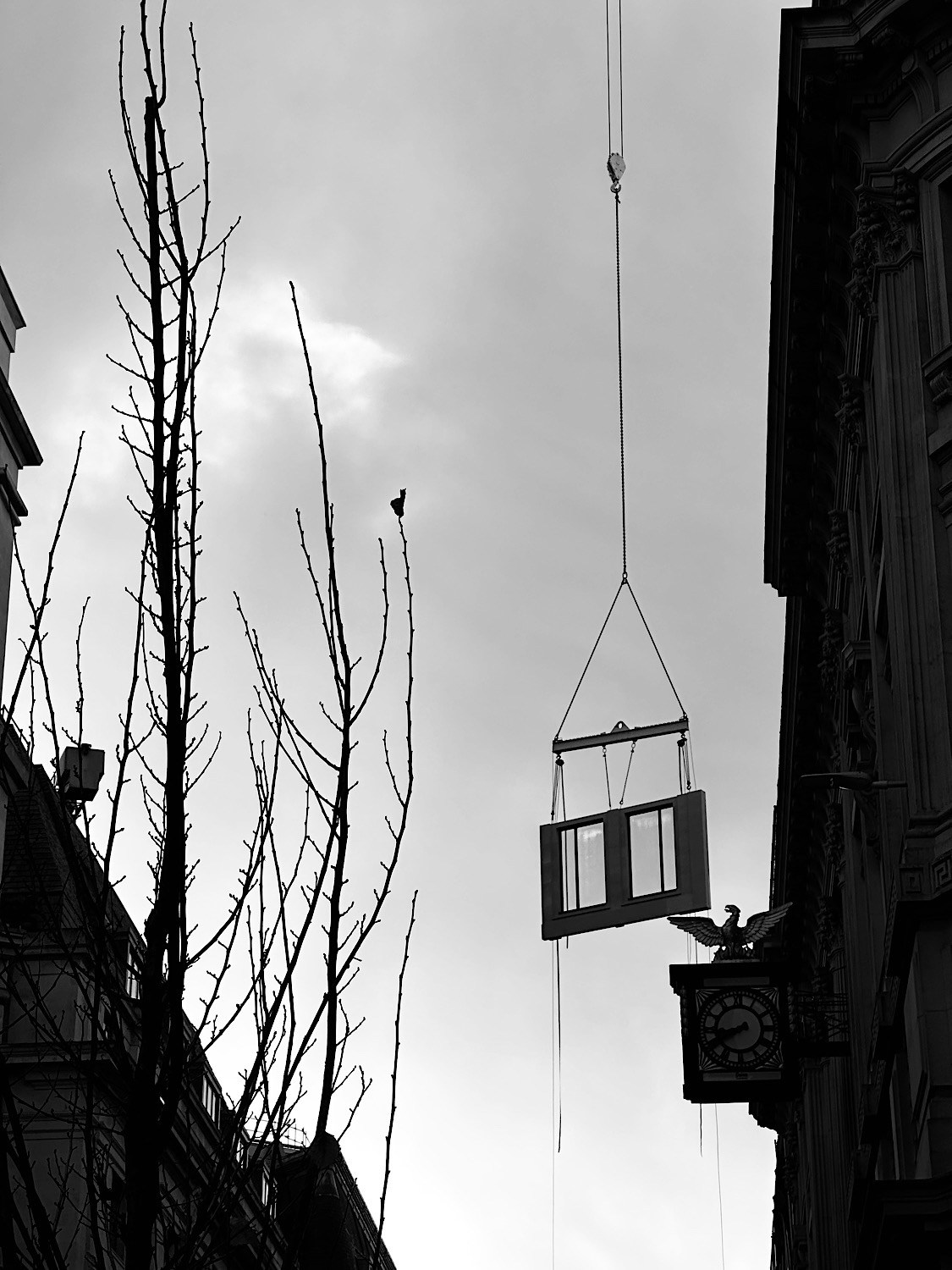 A suspended rectangular frame hangs between tall buildings against a narrow strip of sky.