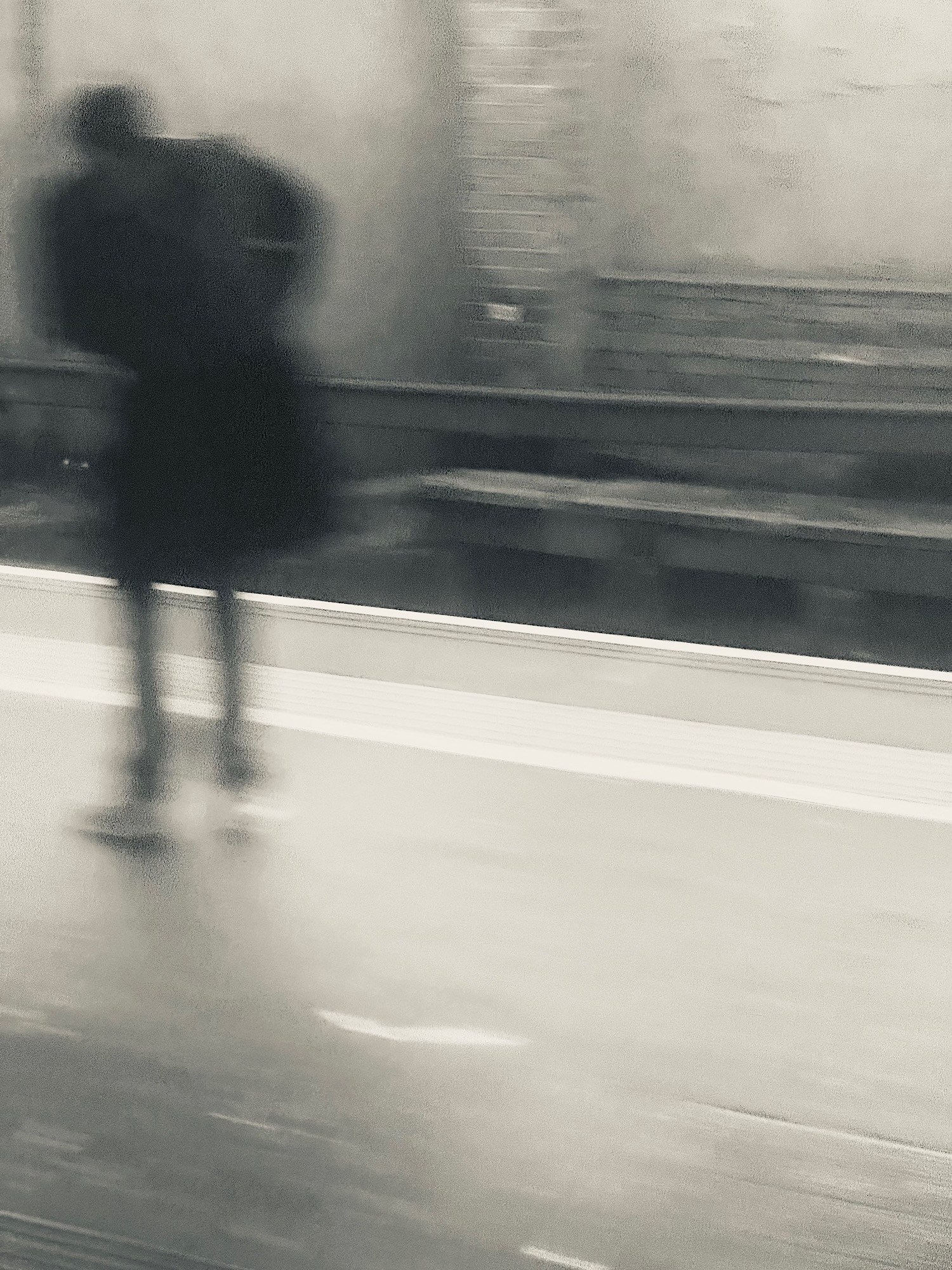 A lone figure stands on a railway platform as the station blurs horizontally around them.