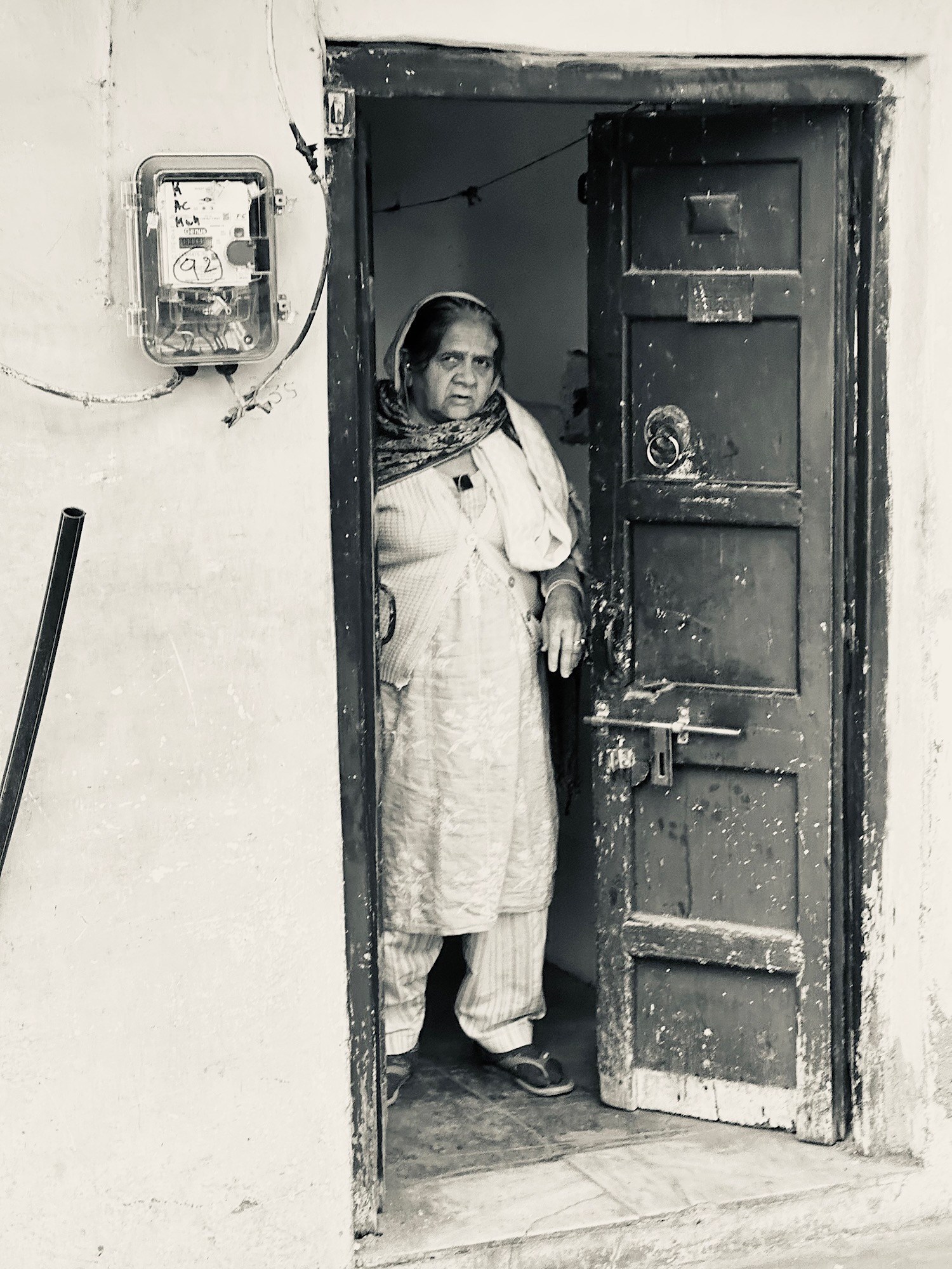 A woman stands in a worn doorway beside an electric meter and pale textured walls.