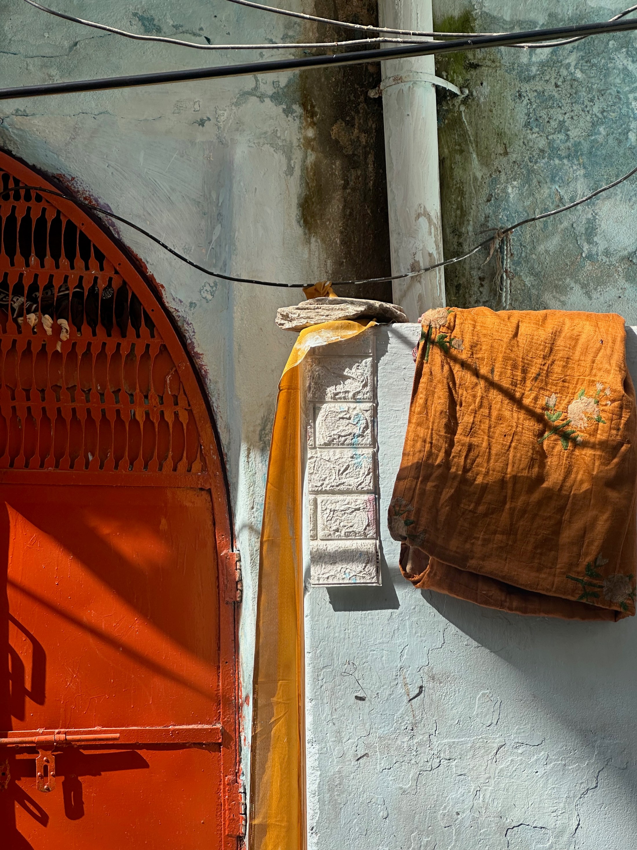 An orange cloth hangs against a blue wall beside a red gate and crossing wires.