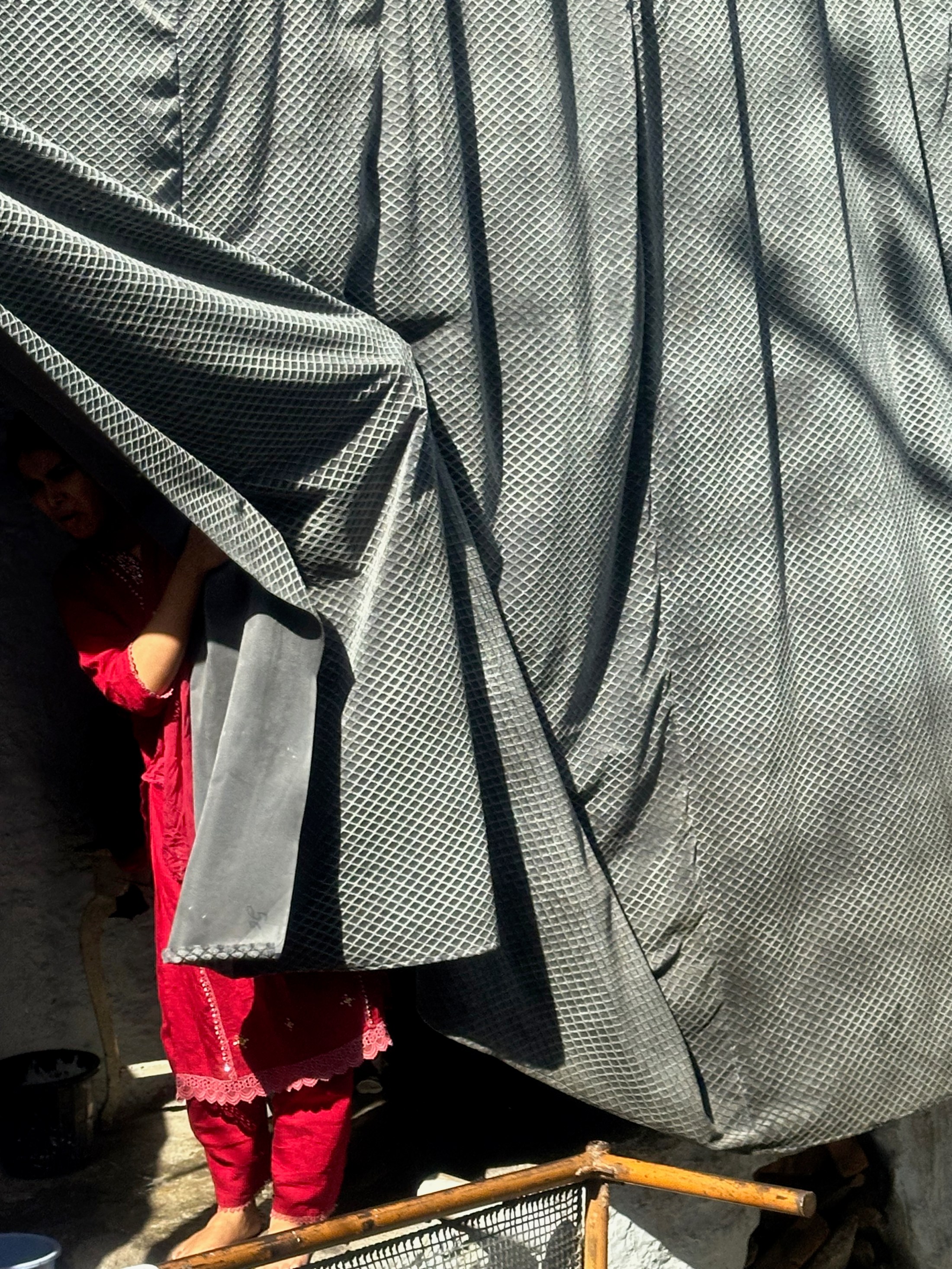 A glimpse of red clothing appears behind a large draped sheet at a street stall.