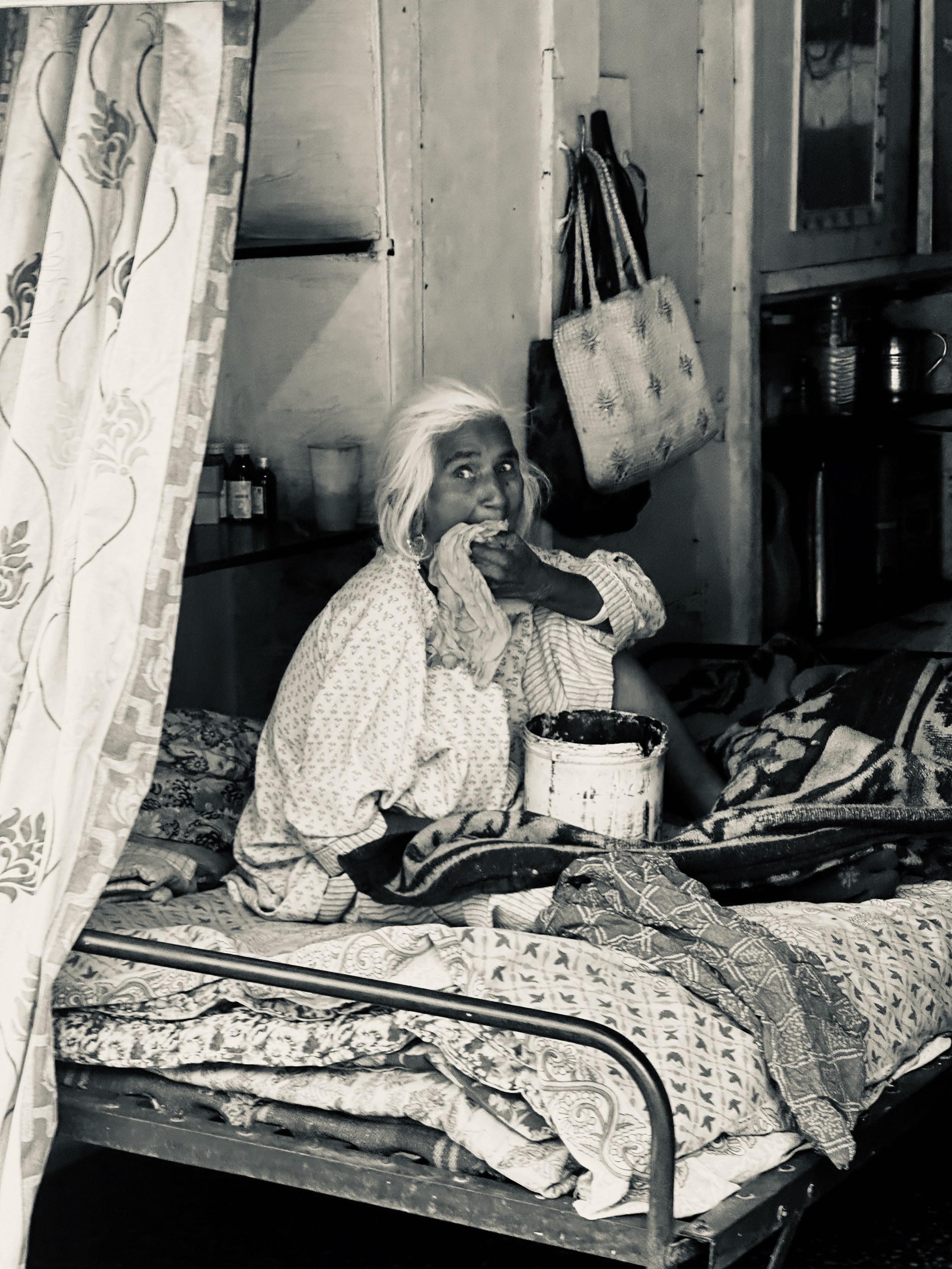 A seated woman holding a cup looks upward from a densely furnished room.