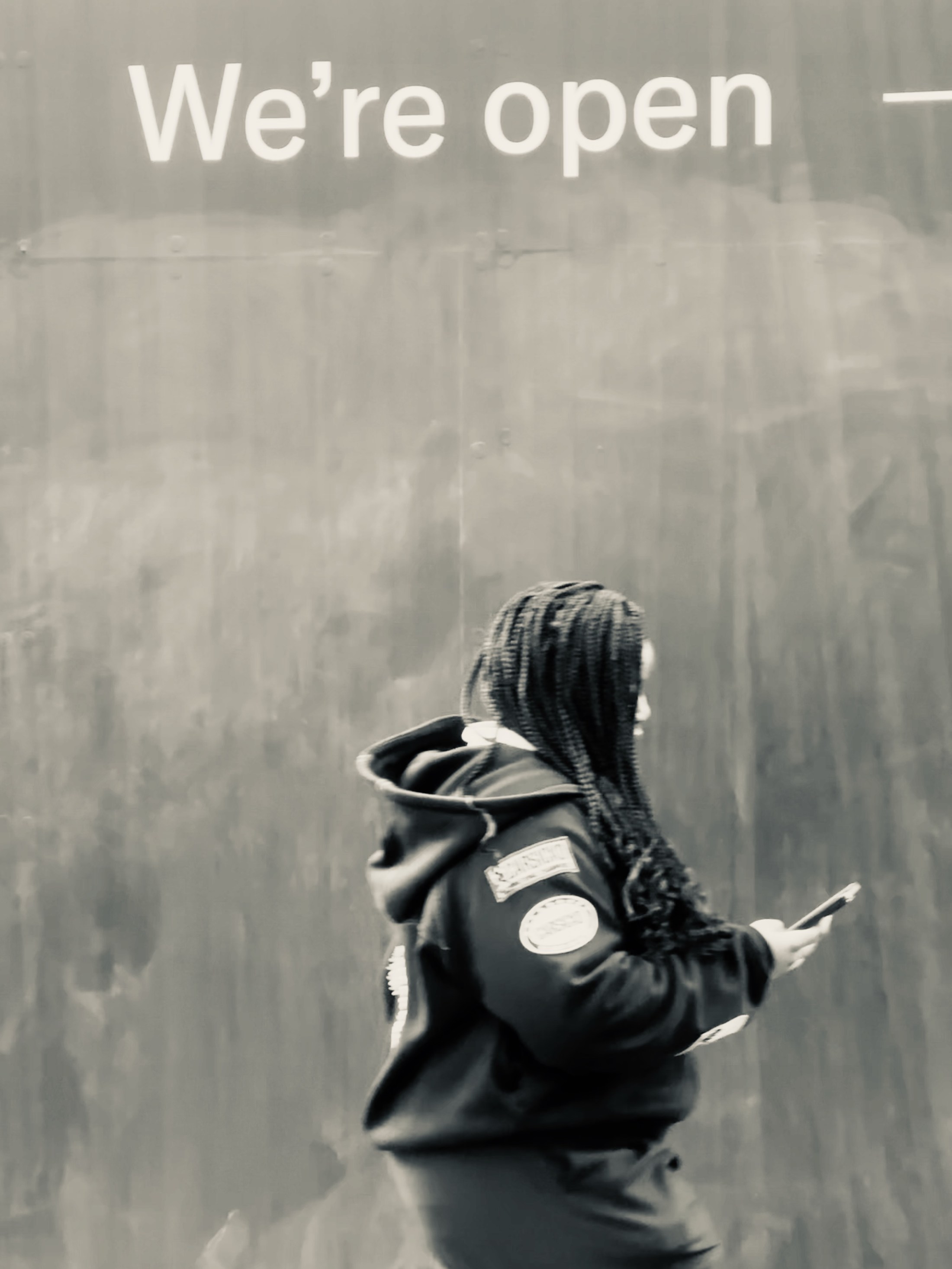 A hooded person looking at a phone beneath the words We’re open.