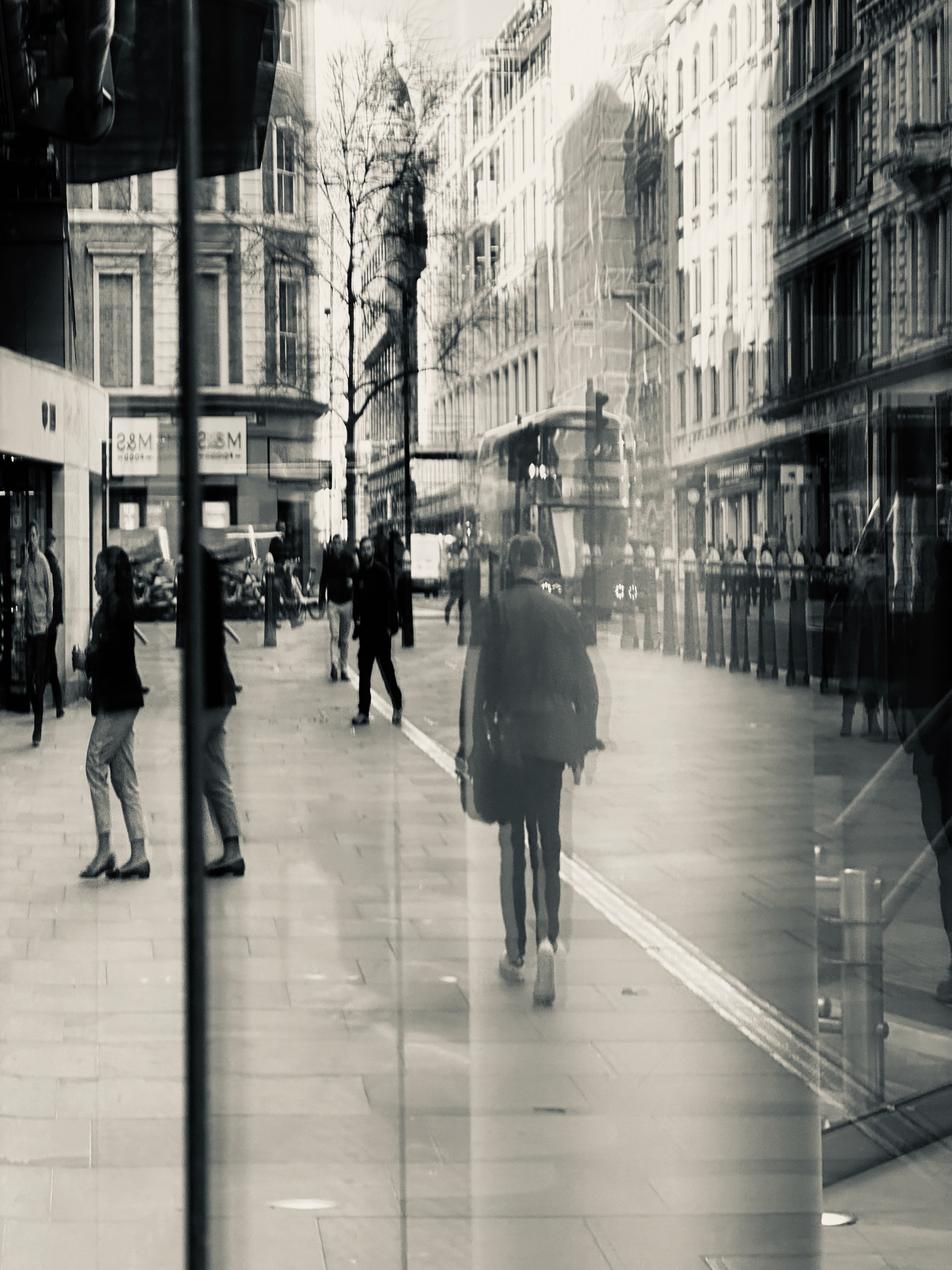 Pedestrians, a bus and shop façades layered in a soft reflection.