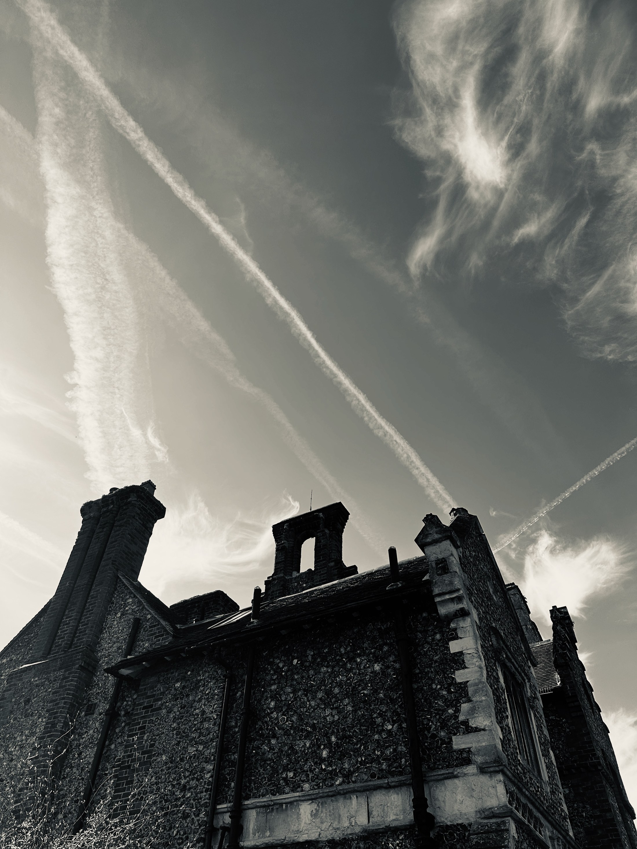 An old roof and chimney pots beneath long crossing contrails.