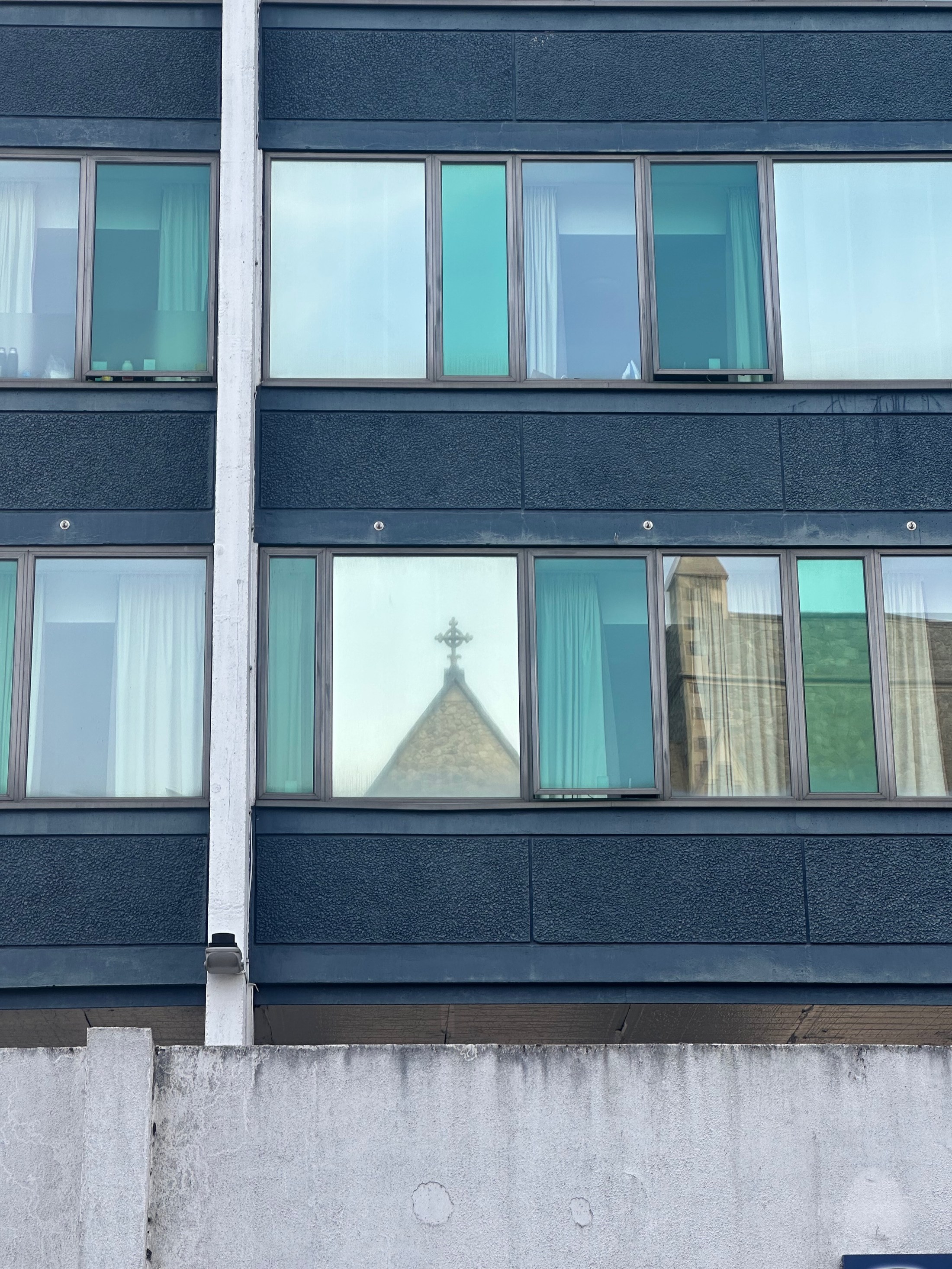 A church spire reflected within a grid of coloured modern windows.