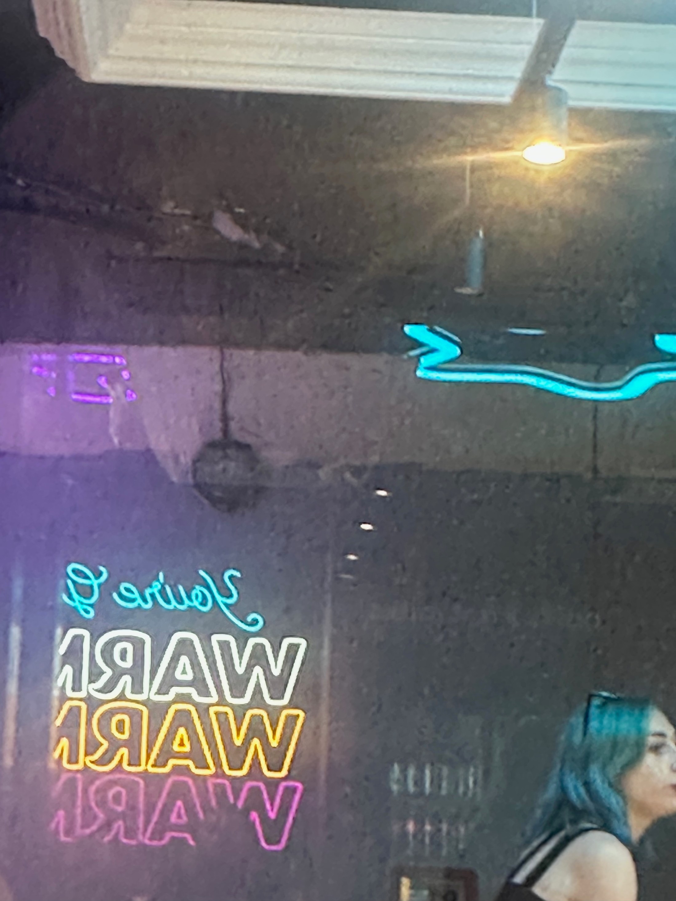 A passing profile beside multicoloured neon lettering reflected in a dark window.